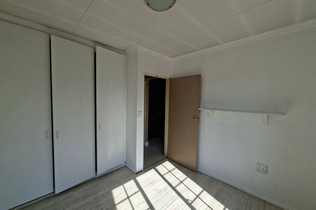 An empty bedroom featuring built-in cupboards, laminate flooring, and a simple wall-mounted shelf, awaiting personal touches.