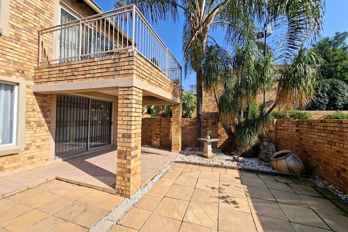 Rear exterior view of the townhouse featuring a paved patio area, a covered balcony with metal railings, and a private brick-walled garden space.