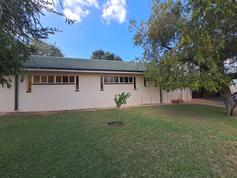 A view of the rear exterior of the house featuring a tiled roof, horizontal windows, a paved walkway, and a well-maintained lawn.