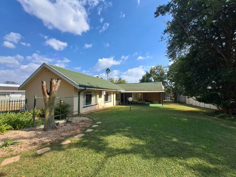 Rear view of the house featuring a green tiled roof, a covered patio area, and a spacious lawn with established garden landscaping.