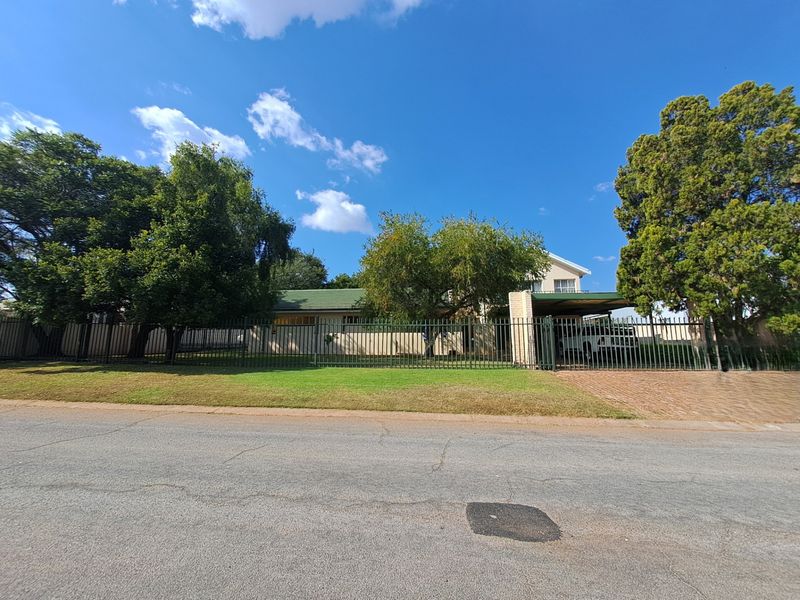 Front view of the property featuring a metal perimeter fence, a paved driveway, and a covered carport area.