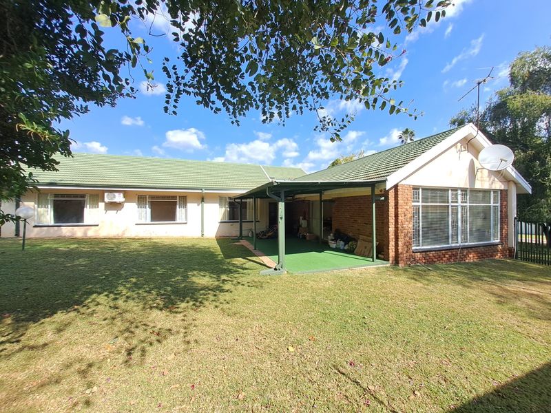 Rear view of the house featuring a tiled roof, brick accents, a covered patio area, and a spacious lawn.