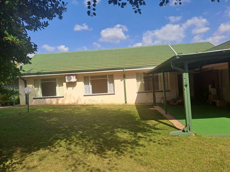 Rear view of the house featuring a tiled roof, a covered patio area, and a well-maintained lawn.