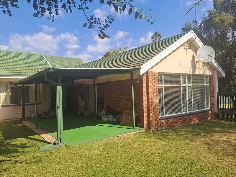 Rear view of the house featuring a covered patio area, brick exterior walls, green tiled roof, and large windows with blinds.