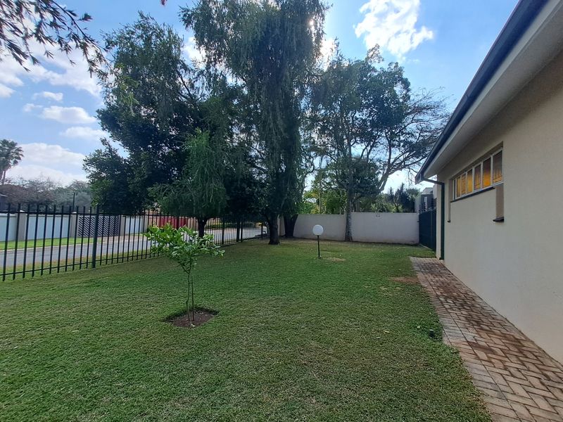 A well-maintained garden area featuring a neat lawn, brick paved pathway, and secure metal perimeter fencing.