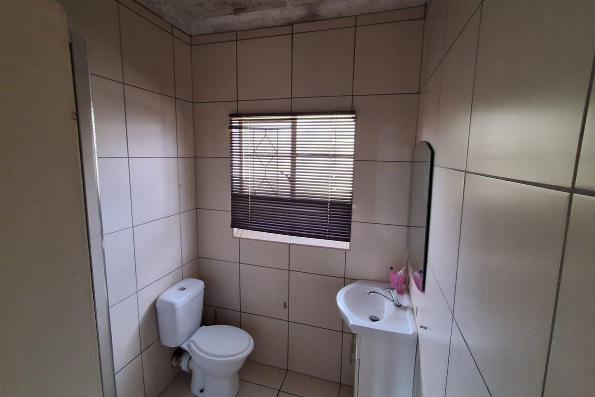 A small bathroom featuring tiled walls and floors, a pedestal basin, and a toilet, requiring ceiling repairs and cosmetic updates.