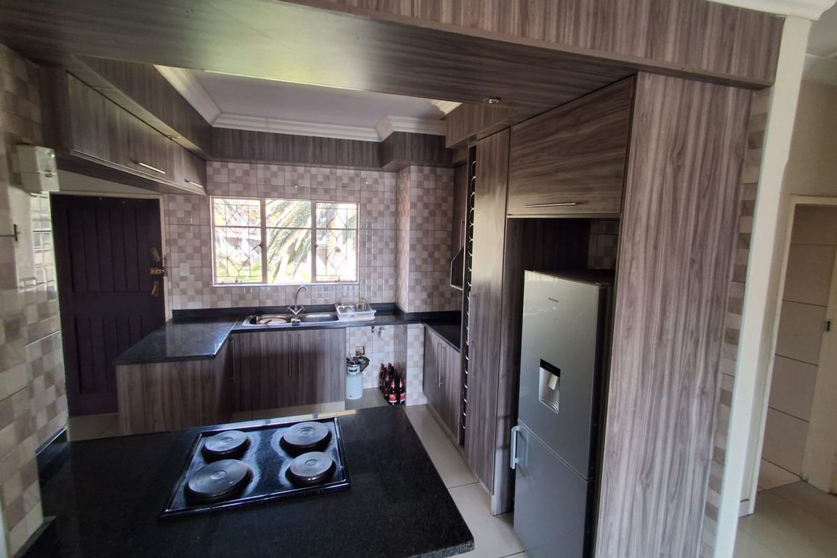 A functional kitchen featuring wood-look laminate cabinetry, granite countertops, a built-in electric hob, and a tiled backsplash with a double basin sink.