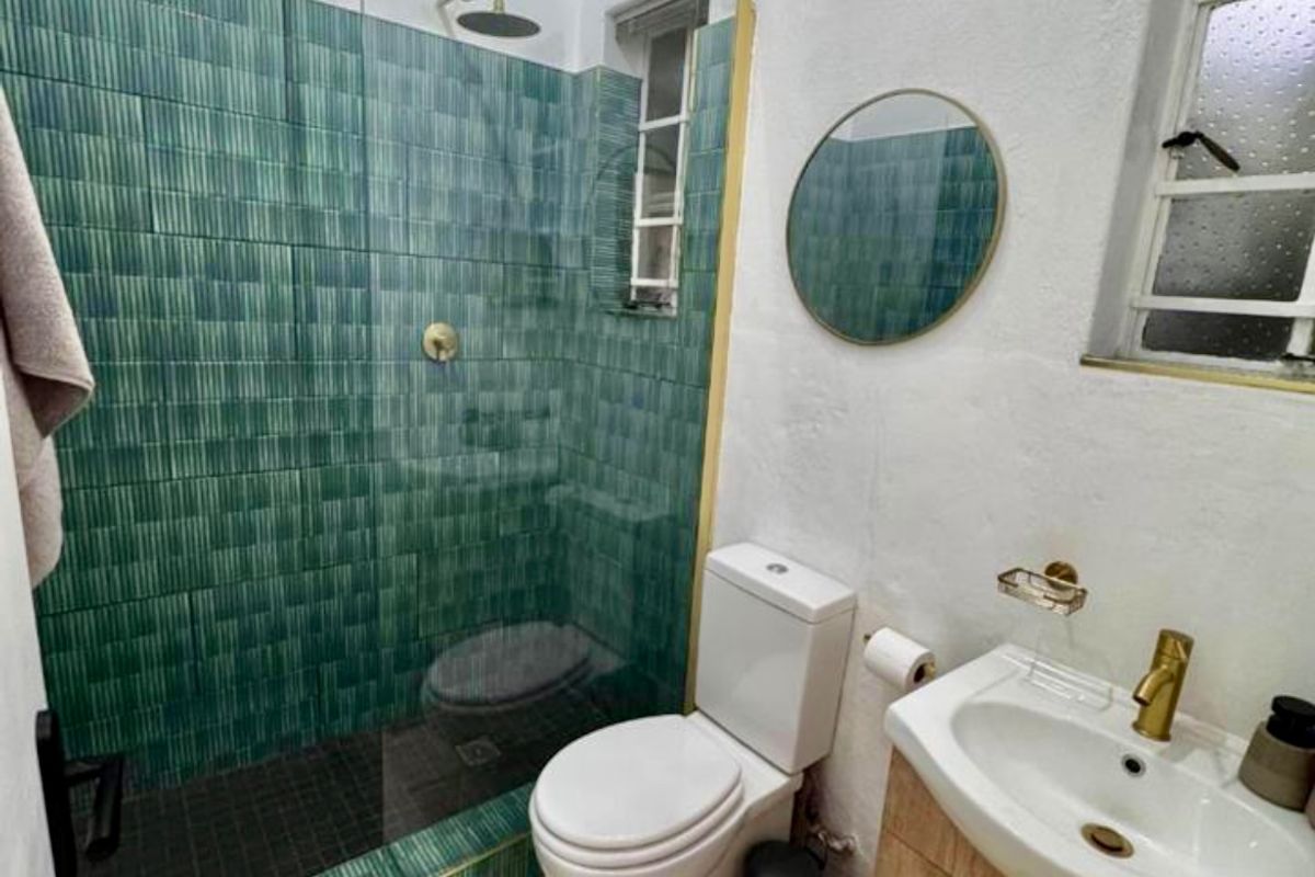 Modern bathroom featuring a walk-in shower with green textured tiles, brass fixtures, a vanity cabinet, and a toilet.