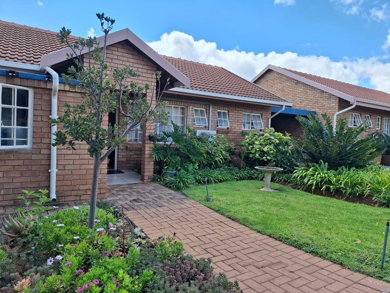 Front view of a brick townhouse featuring a paved walkway, well-maintained garden, and tiled roof.