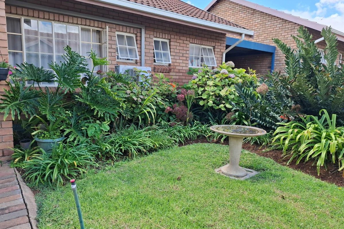 A well-maintained rear garden area featuring a brick townhouse facade, established landscaping, and a small lawn.