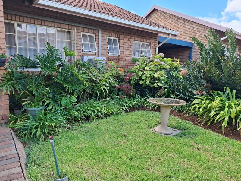 A well-maintained rear garden area featuring a brick townhouse facade, established landscaping, and a small lawn.