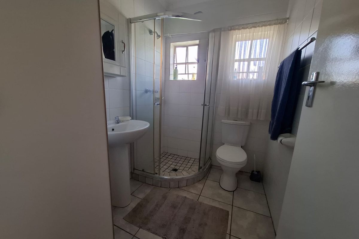 A functional bathroom featuring a corner shower enclosure, pedestal basin, and toilet with neutral wall and floor tiling.