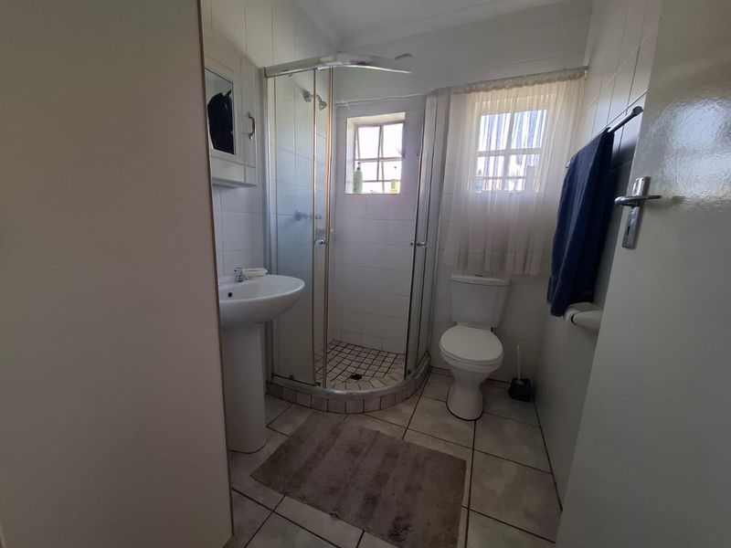 A functional bathroom featuring a corner shower enclosure, pedestal basin, and toilet with neutral wall and floor tiling.