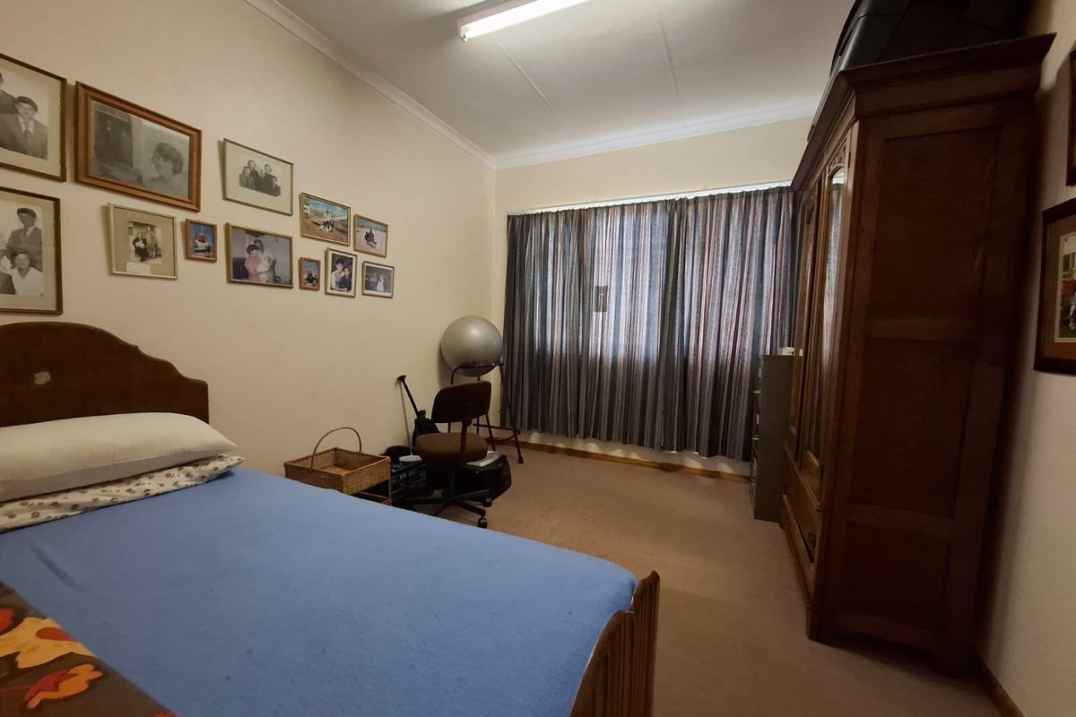 A standard bedroom featuring neutral walls, carpeted flooring, and a large window with installed curtain tracks.