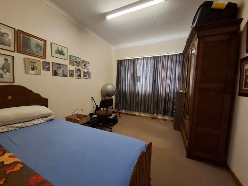 A standard bedroom featuring neutral walls, carpeted flooring, and a large window with installed curtain tracks.