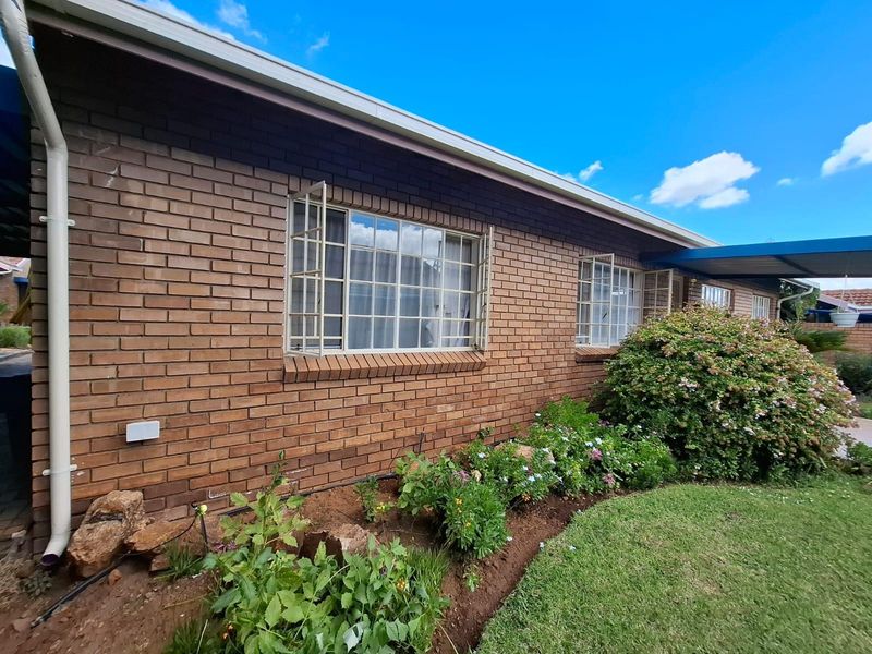 Rear exterior view of the townhouse featuring a classic brick facade, steel casement windows with security bars, and a well-maintained garden area.