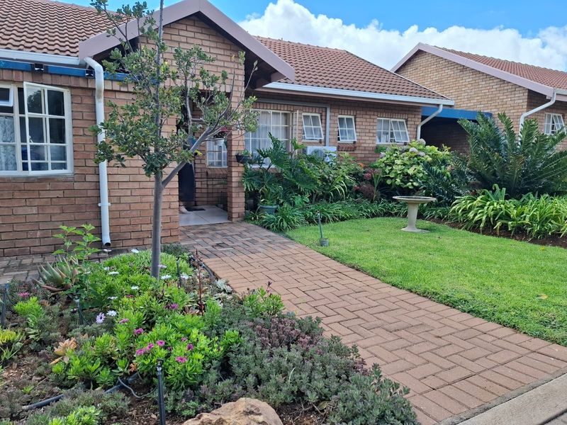 A well-maintained townhouse front elevation featuring a classic brick facade, tiled roof, and a neatly landscaped garden with a paved entrance walkway.