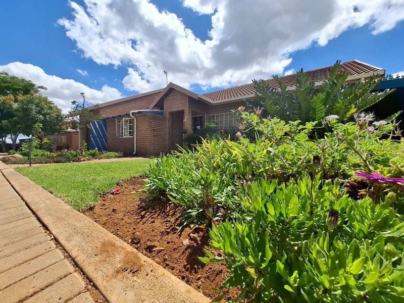Front view of a brick townhouse featuring a well-maintained garden, paved walkway, and tiled roof under a clear blue sky.