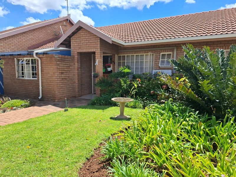 Front elevation of a face brick townhouse featuring a tiled roof, paved walkway, and established garden with a secure entrance.