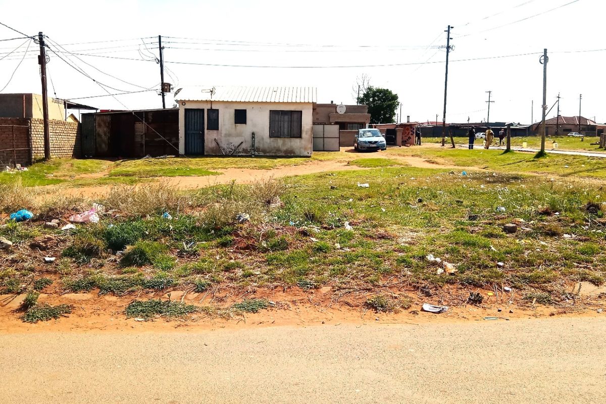 A view of a residential property exterior featuring a small structure with a corrugated metal roof and surrounding unmaintained land.