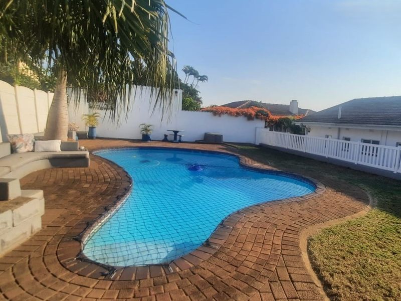 Outdoor pool area featuring a kidney-shaped swimming pool, brick paved surround, built-in concrete seating, and white boundary fencing.