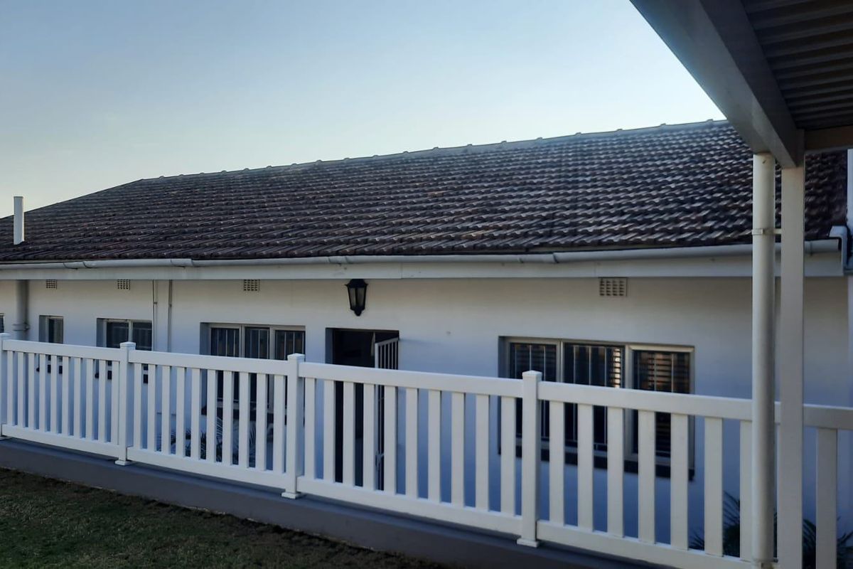 A view of the rear exterior of the house featuring a tiled roof, white picket fence, and a covered patio area.