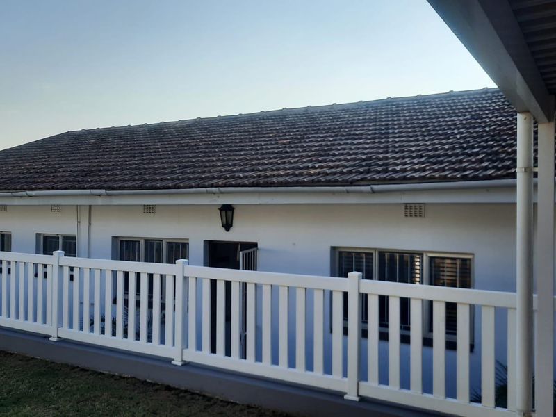 A view of the rear exterior of the house featuring a tiled roof, white picket fence, and a covered patio area.