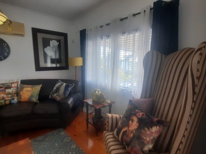 A cozy living room featuring polished timber flooring, a wall-mounted split system air conditioner, and window shutters for natural light control.