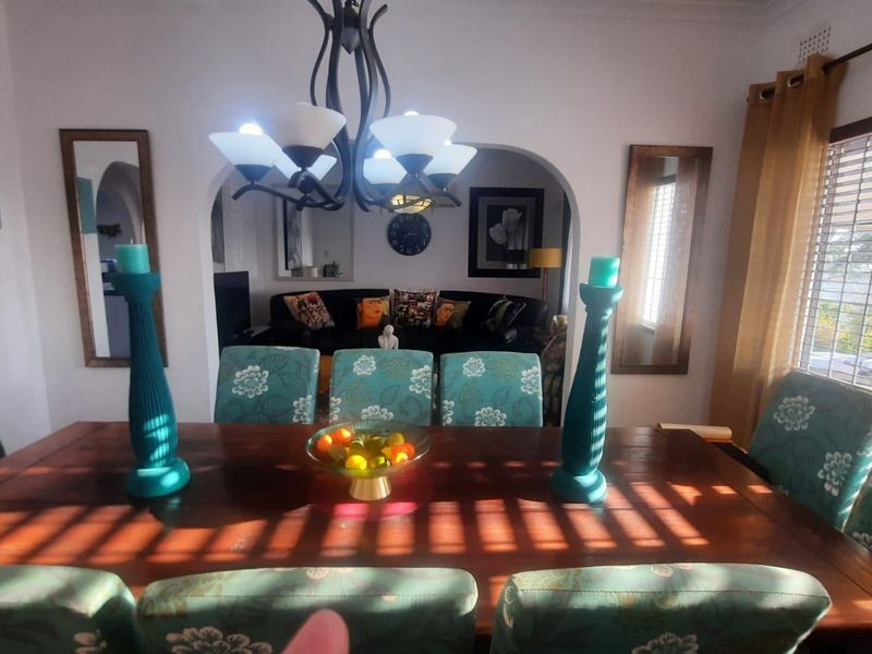 Dining room featuring an arched entryway leading to an adjacent living space, illuminated by a central chandelier and natural light through window blinds.