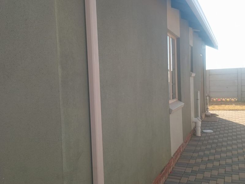 A side view of the property exterior featuring a paved walkway, downpipe, and a precast concrete boundary wall.