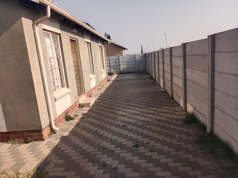 A paved side yard area featuring a precast concrete boundary wall and exterior access to the house.