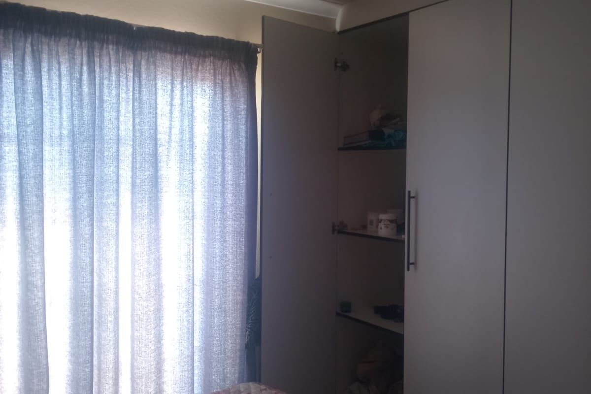 A bedroom featuring a built-in wardrobe with shelving and a window dressed with curtains.