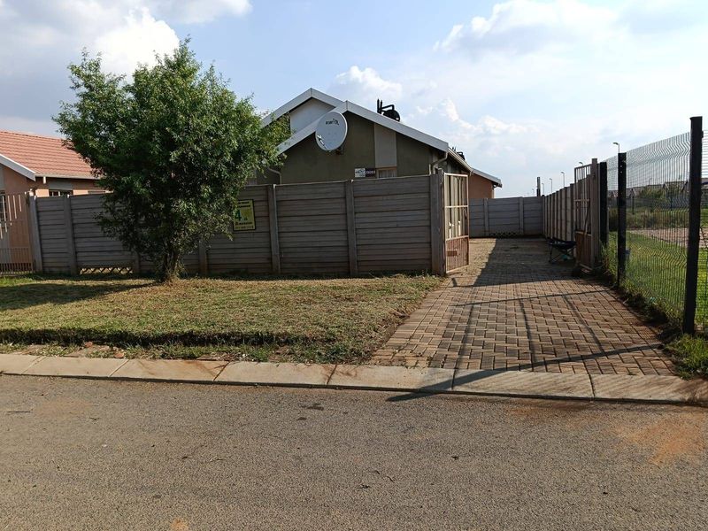 Front exterior view of the property featuring a paved driveway, precast concrete boundary wall, and metal gate access.