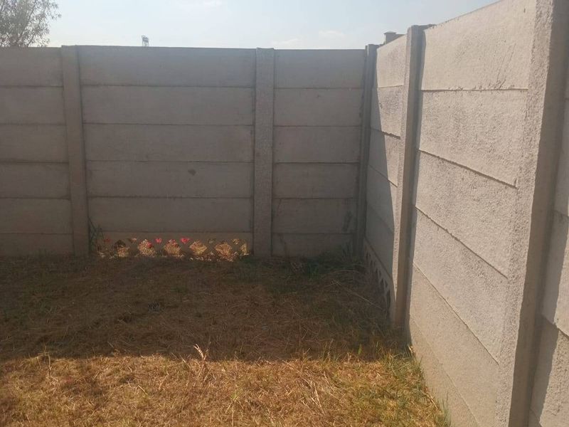 A small, private garden area enclosed by precast concrete boundary walls, featuring a paved section and a dry lawn requiring maintenance.