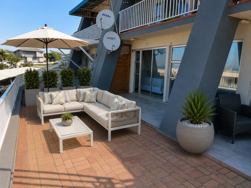 A spacious outdoor balcony featuring brick-style paving, metal railings, and direct access to the interior through large sliding glass doors.
