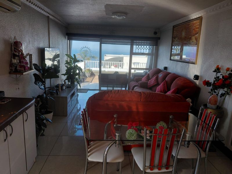 Open-plan living and dining area featuring tiled floors, decorative ceiling cornices, and large sliding glass doors leading to an outdoor balcony with ocean views.