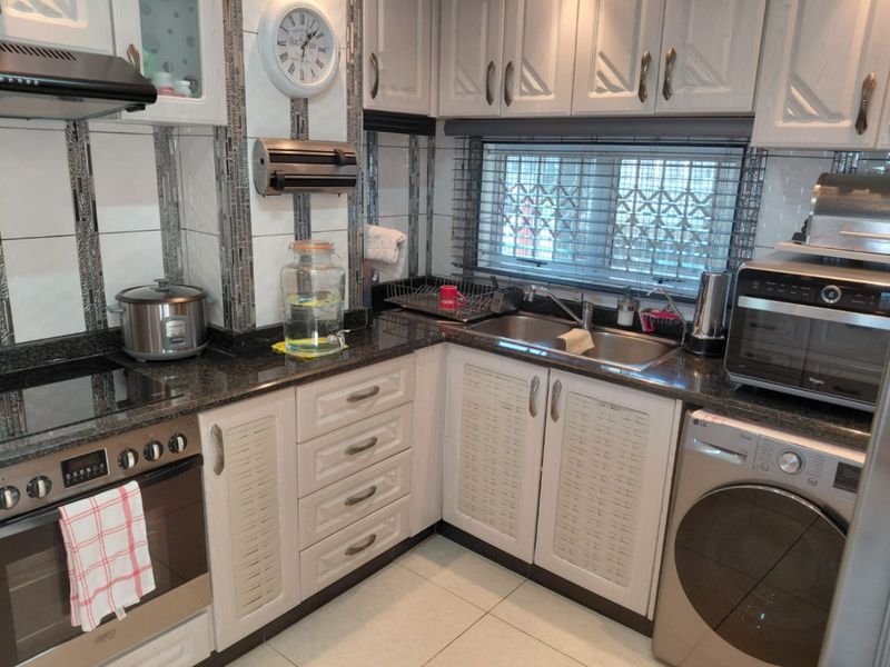 Compact kitchen featuring granite countertops, built-in cabinetry, integrated oven and hob, and a double sink with a window security gate.
