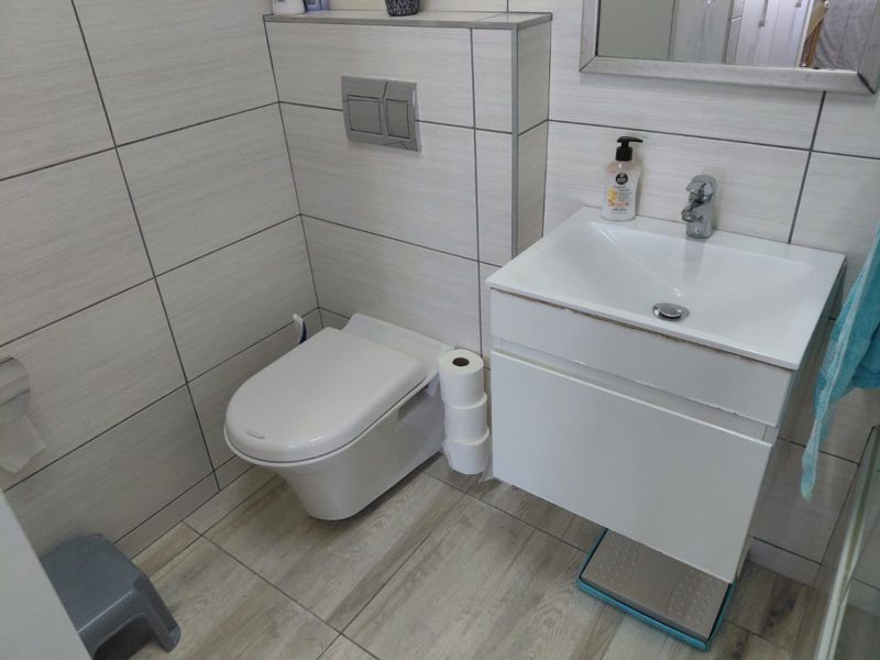 A compact modern bathroom featuring a wall-hung toilet with a concealed cistern and a white vanity basin with tiled finishes.