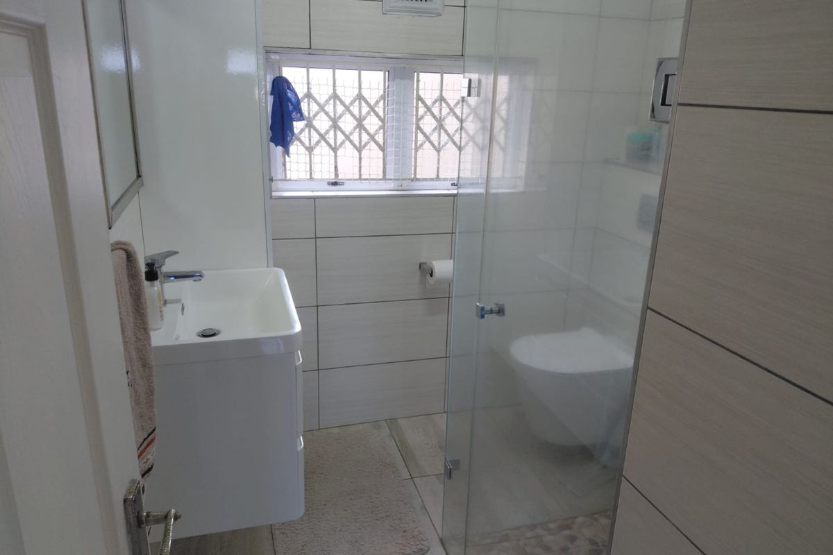 A modern bathroom featuring a wall-mounted vanity, glass-enclosed shower, and neutral tiled finishes with a secure window.