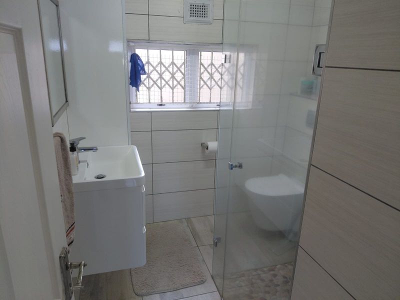 A modern bathroom featuring a wall-mounted vanity, glass-enclosed shower, and neutral tiled finishes with a secure window.