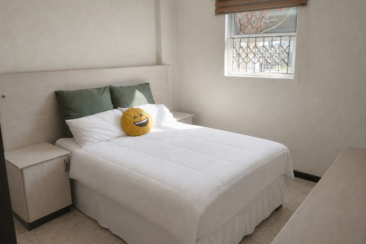 A functional bedroom featuring built-in bedside tables, a matching headboard, tiled flooring, and a window fitted with a security gate and roller blind.