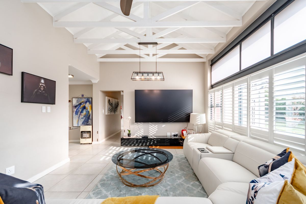 Spacious living room featuring a high vaulted ceiling with exposed white timber trusses, tiled flooring, and plantation shutters allowing for ample natural light.