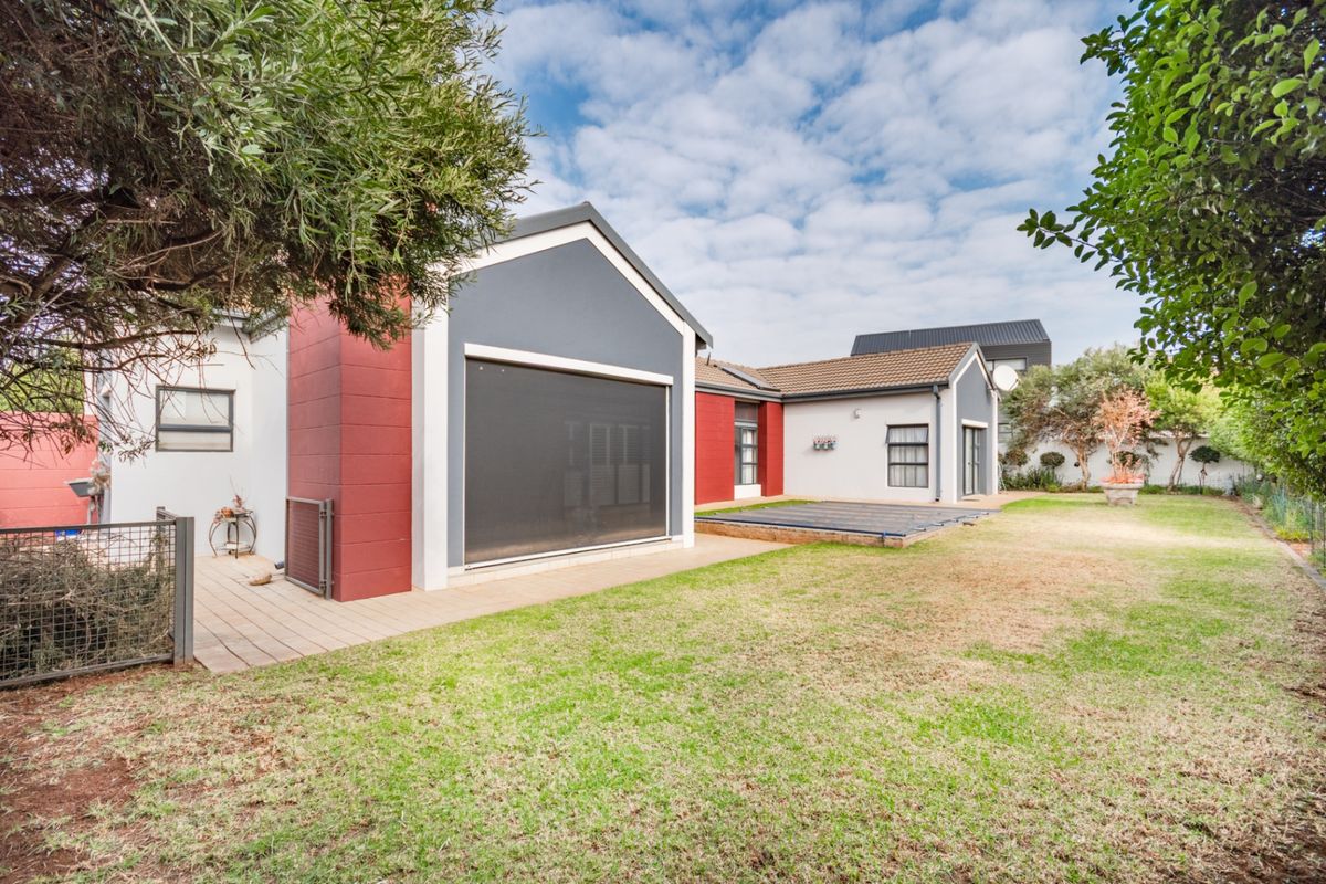 Rear view of the property featuring a landscaped garden, paved decking area, and a swimming pool with a protective cover.