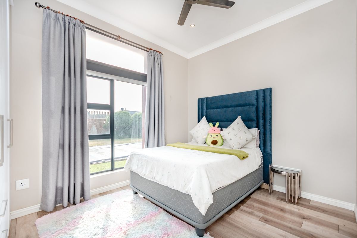 A bright and modern bedroom featuring laminate flooring, a large window with curtains, recessed lighting, and a ceiling fan.