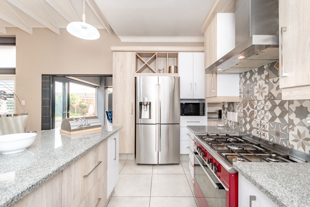 Modern kitchen featuring granite countertops, a gas stove with extractor fan, patterned tile backsplash, and light wood cabinetry with integrated wine storage.