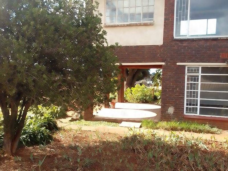 Rear view of a two-story brick house featuring a covered patio area and established garden space.