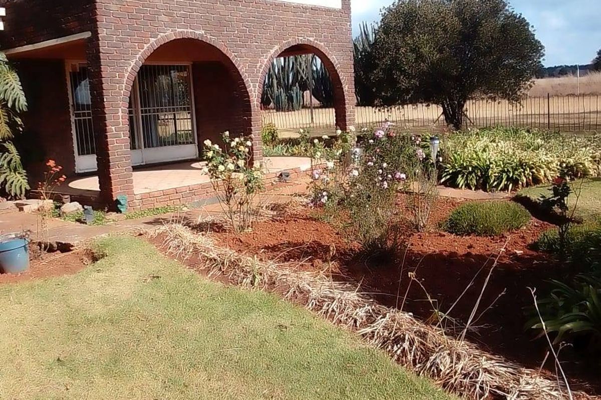 A two-story brick house featuring an arched ground-floor patio, an upper-level balcony, and a landscaped garden area.