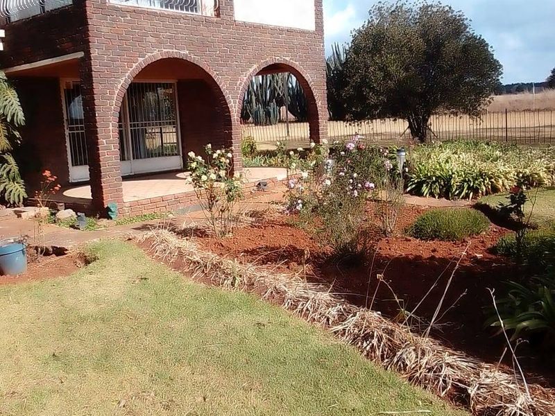 A two-story brick house featuring an arched ground-floor patio, an upper-level balcony, and a landscaped garden area.