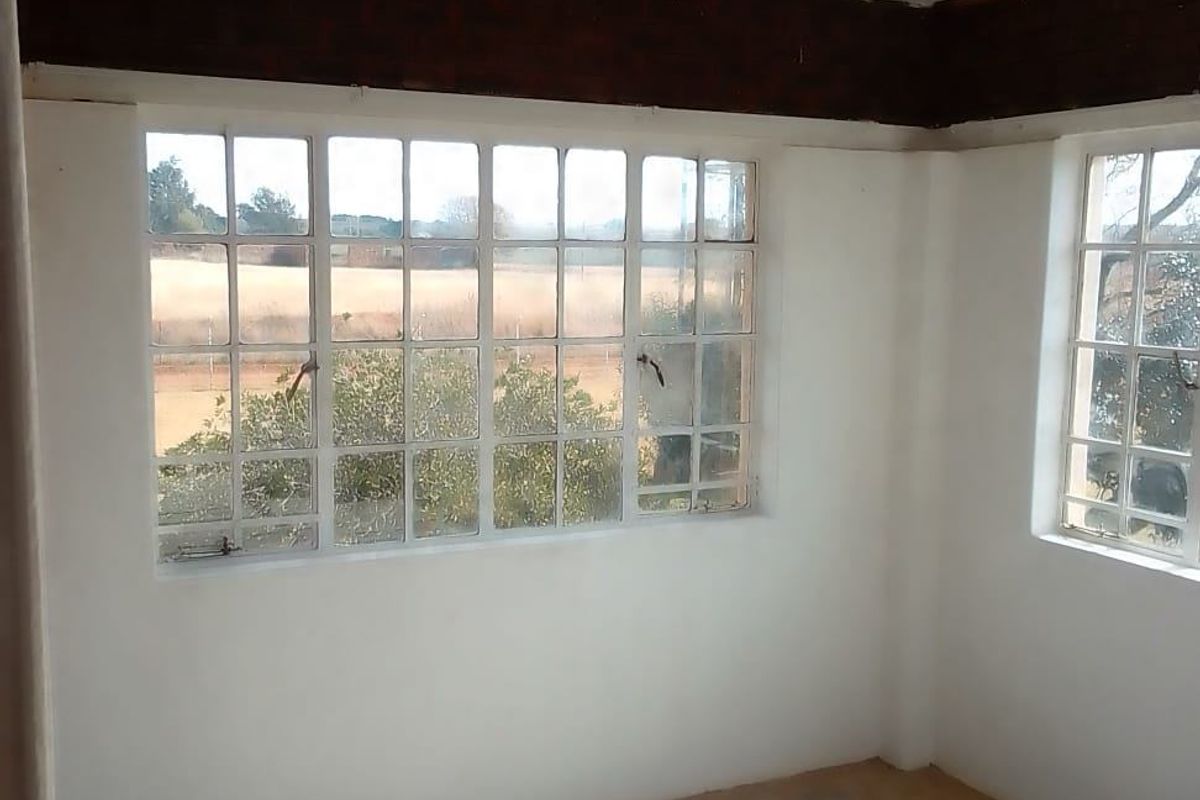 An empty bedroom featuring steel-framed windows and an exposed timber beam, offering a blank canvas for renovation.
