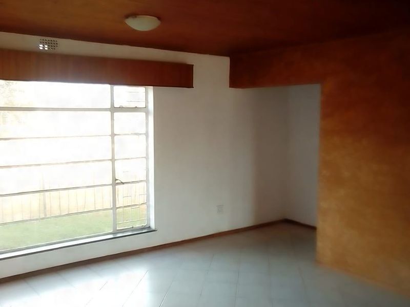 An empty living room featuring tiled flooring, a large window, and a distinctive timber ceiling with a textured feature wall.